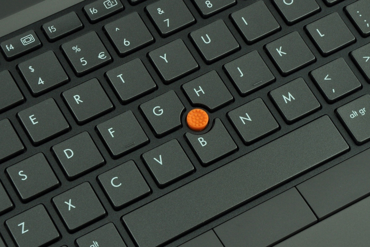 Close-up of a dark laptop keyboard with an orange TrackPoint pointing stick between the G and H keys.