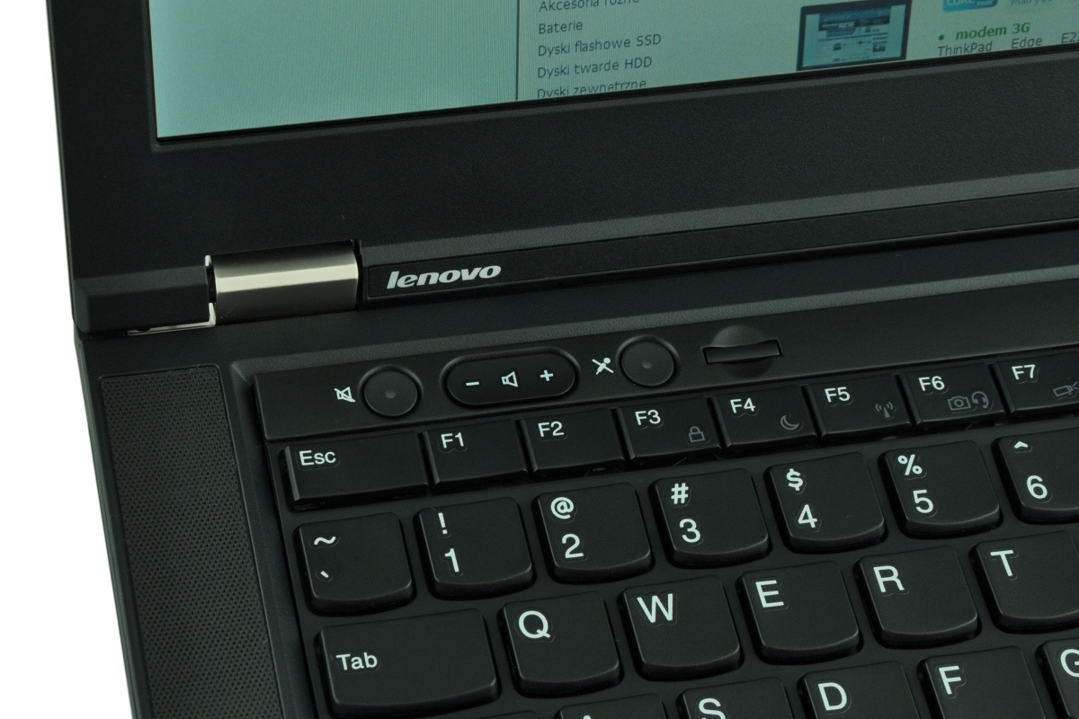 Close-up of a black Lenovo laptop keyboard and hinge area, shows logo on the lid and function keys F1–F7 nearby.