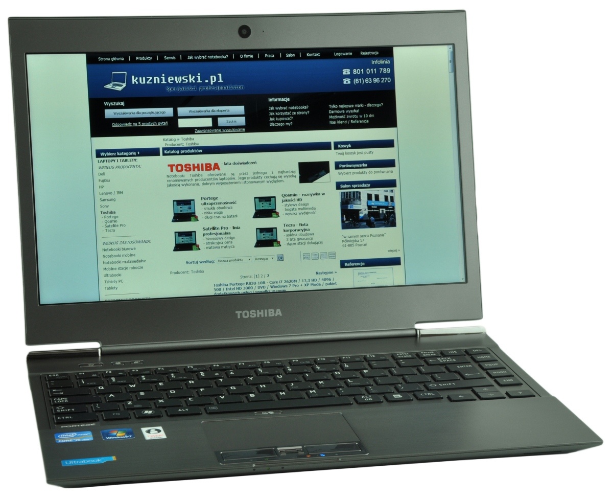 Toshiba laptop on a white surface displaying a Polish website with a blue header and product grid on the screen.