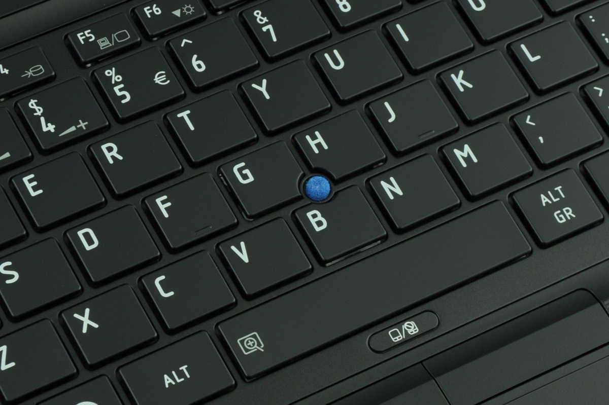 Close-up of a black laptop keyboard with a blue trackpoint nub between the G and B keys.