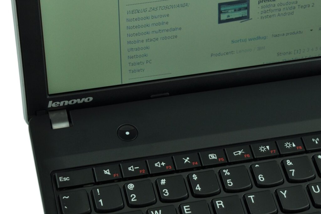 Close-up of a Lenovo laptop keyboard and hinge with a screen showing a blurred webpage
