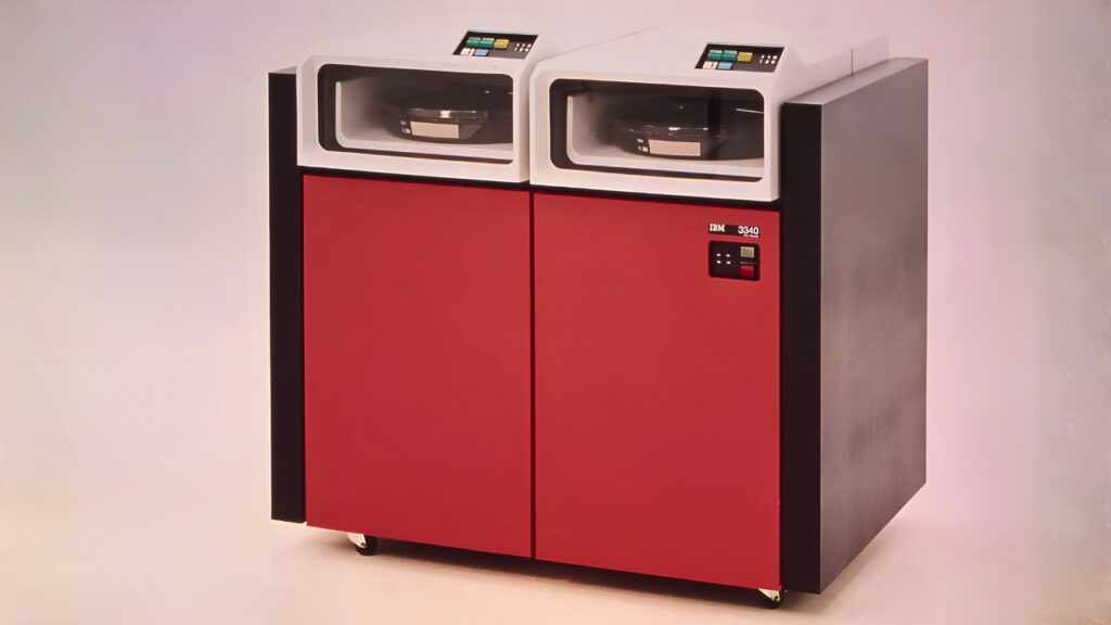 Vintage IBM 3340 tape storage unit with two tape drives on top and red two-door cabinet below, on wheels.