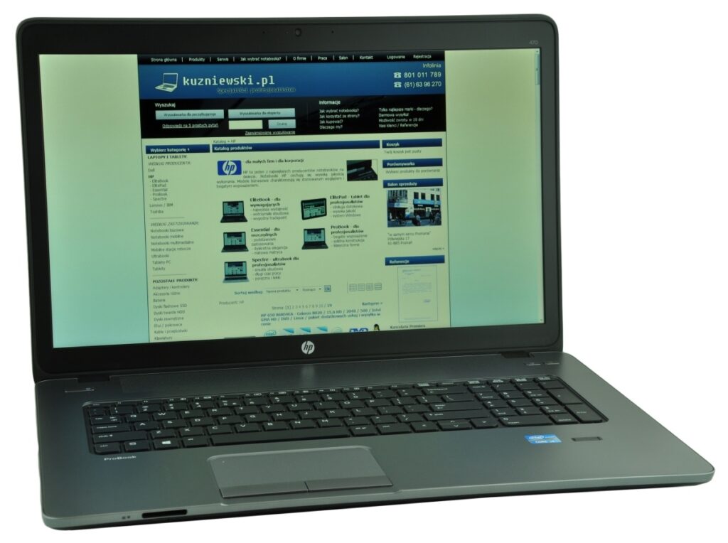 HP laptop open, showing a Polish tech website on the screen (kuzniewski.pl) with a blue header and sidebar content, on a light-green background.