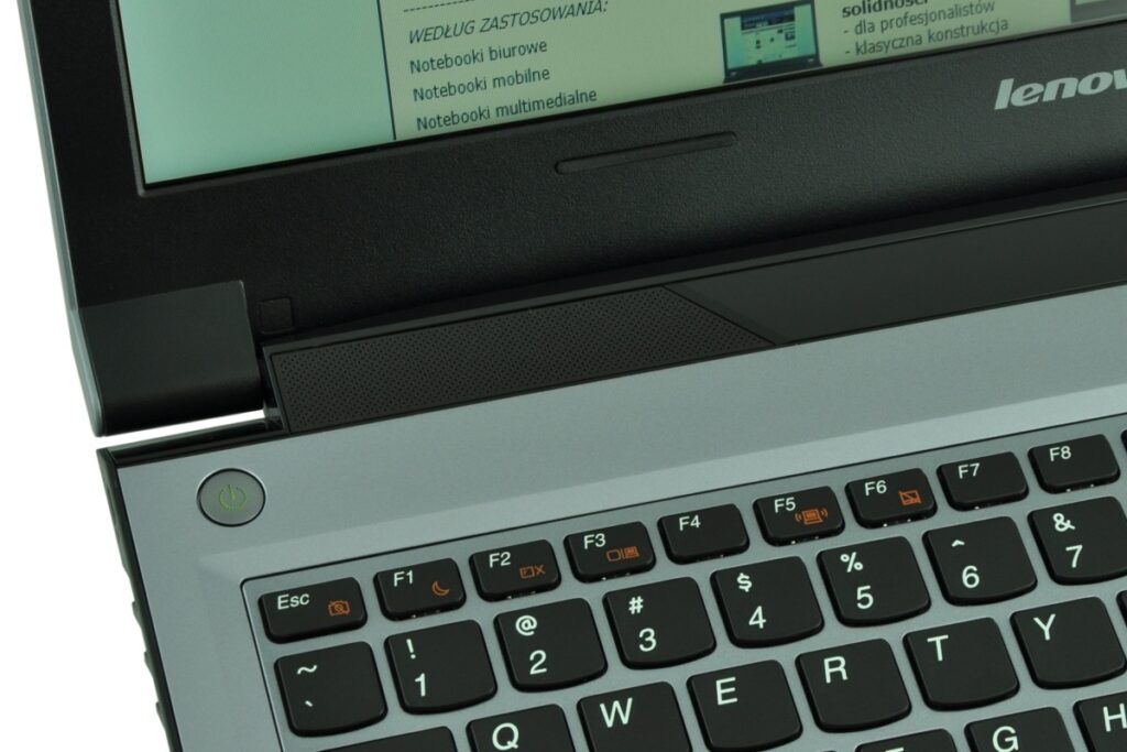 Close-up of a Lenovo laptop keyboard and hinge with a round power button on the left and a partially opened screen above.
