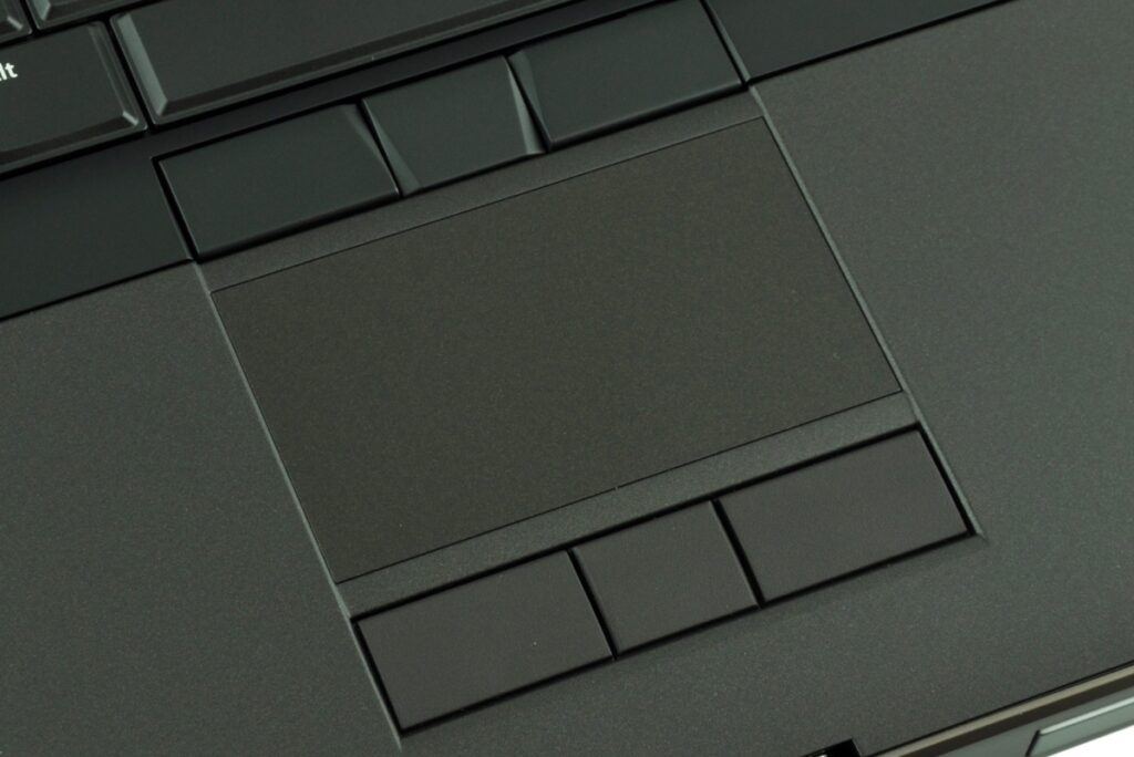dell-precision-m6800-516_125150 - lab-kuzniewski.pl - Testy laptopów, recenzje i porównania Close-up of a dark laptop touchpad surrounded by rectangular buttons on a matte surface