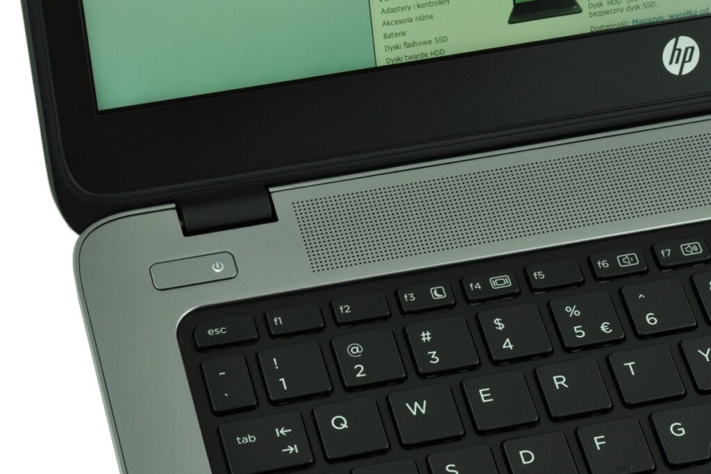 Close-up of a grey HP laptop's upper keyboard area, showing the power button, hinge, speaker grille, and part of the keyboard.