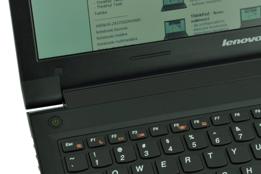 lenovo-b5400-59-399267-c_125508 - lab-kuzniewski.pl - Testy laptopów, recenzje i porównania Close-up of a Lenovo laptop keyboard and power button with a green power icon visible near the hinge. The screen shows a teal display with text and images.