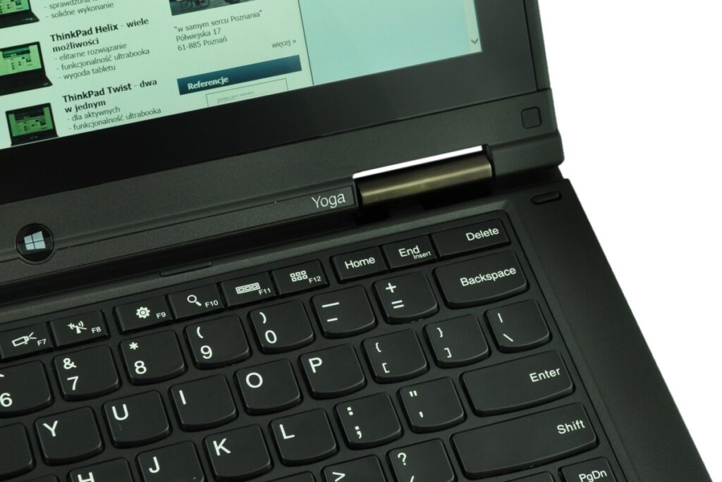 Close-up of a black Lenovo ThinkPad Yoga laptop: keyboard, track area, and screen showing a webpage in Polish.