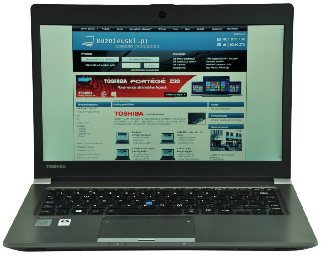 Toshiba laptop open, showing a Polish tech website on the screen with blue header and product banners.