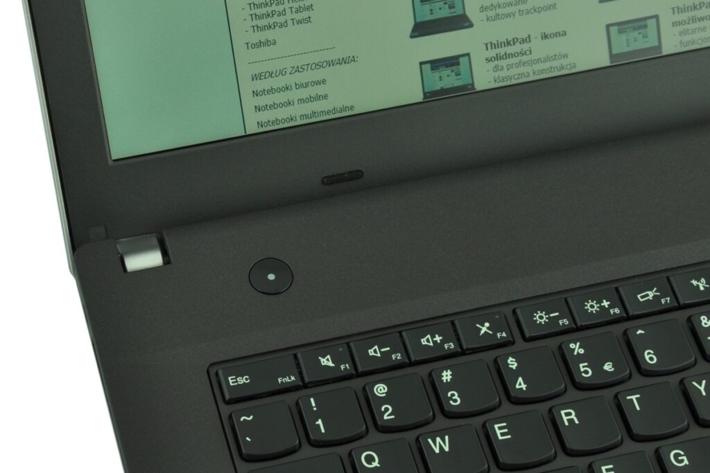 Close-up of a black laptop keyboard (ThinkPad style) with a round button on the palm rest and a green-tinted screen showing a document edge.
