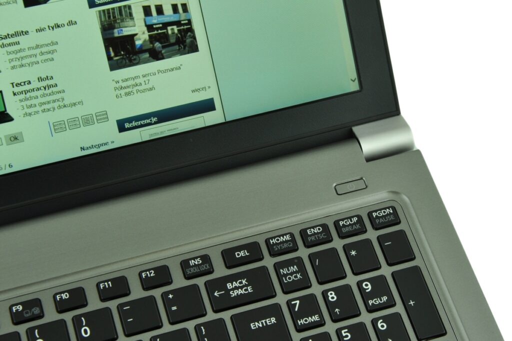 Close-up of a silver laptop with a black keyboard and a Polish website visible on the screen in the background.