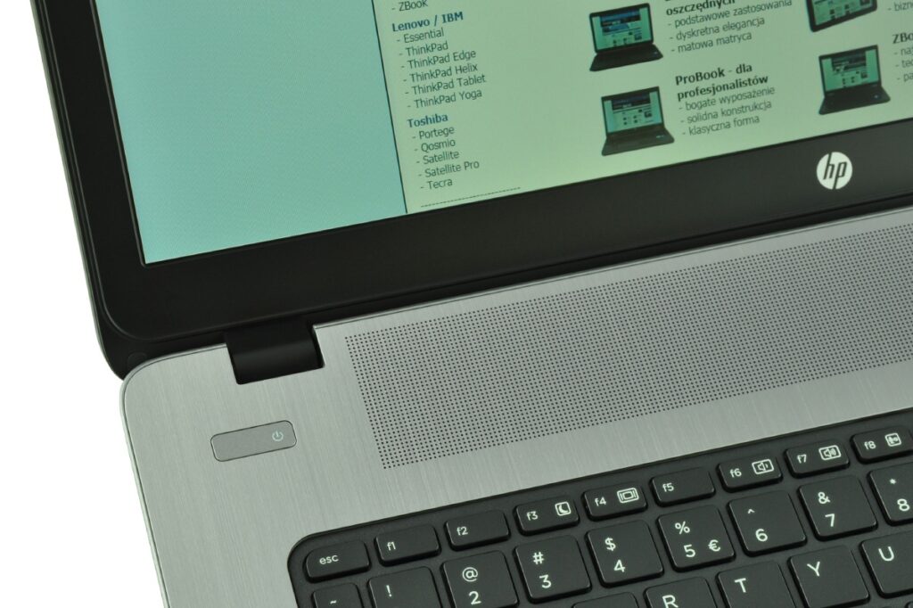 Close-up of an HP laptop open, showing the hinge, metal speaker grille, and part of the keyboard area.