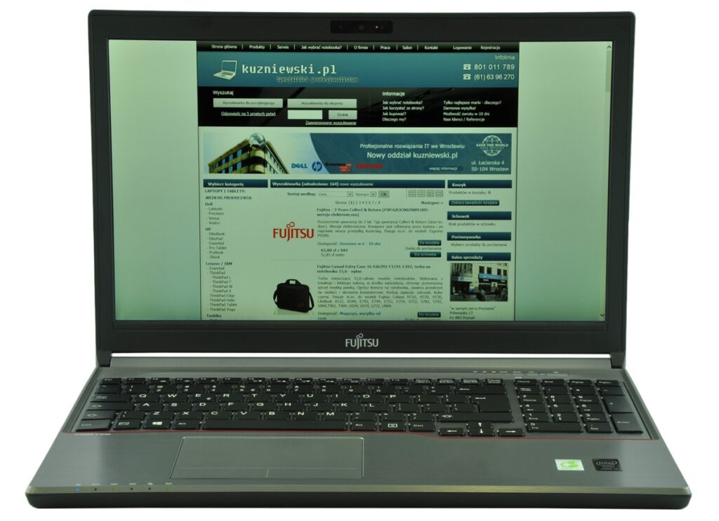Open Fujitsu laptop showing a website page on its screen (kuzniewski.pl) with a black keyboard and silver chassis, angled toward viewer.