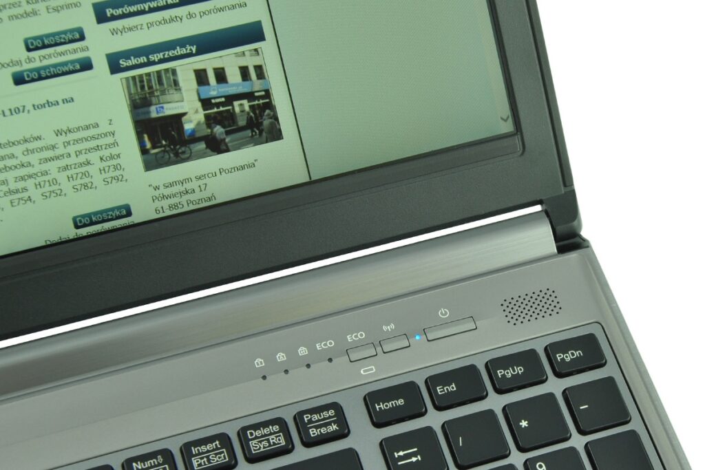 Laptop with a green website page on the screen displaying Polish navigation labels like 'Do koszyka' and 'Salon sprzedaży', and a visible keyboard in the foreground.