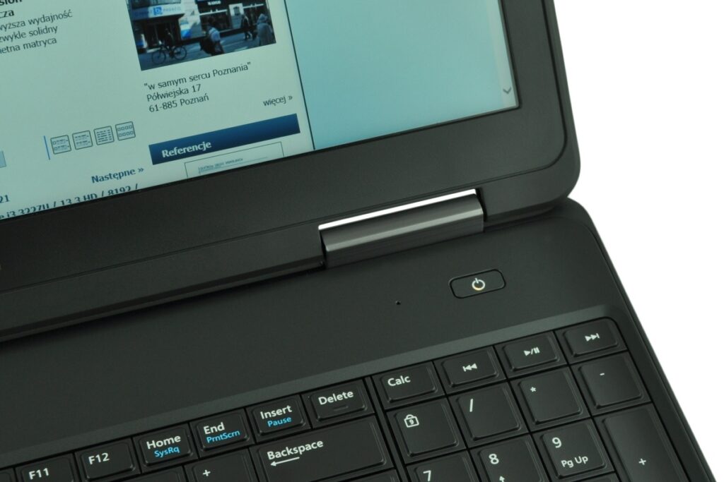 dell-latitude-e5540-5197_125703 - lab-kuzniewski.pl - Testy laptopów, recenzje i porównania Close-up of a black laptop with a screen displaying a Polish webpage; silver hinge and power button visible.