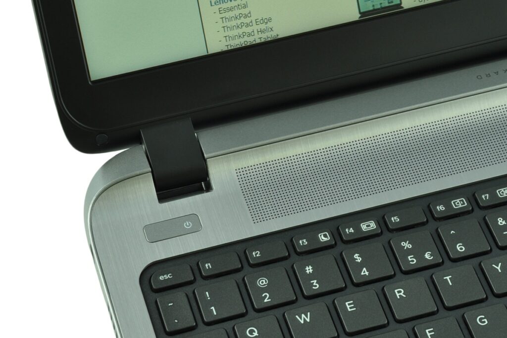 Close-up of a silver laptop corner showing the power button, hinge, and keyboard with black keys.