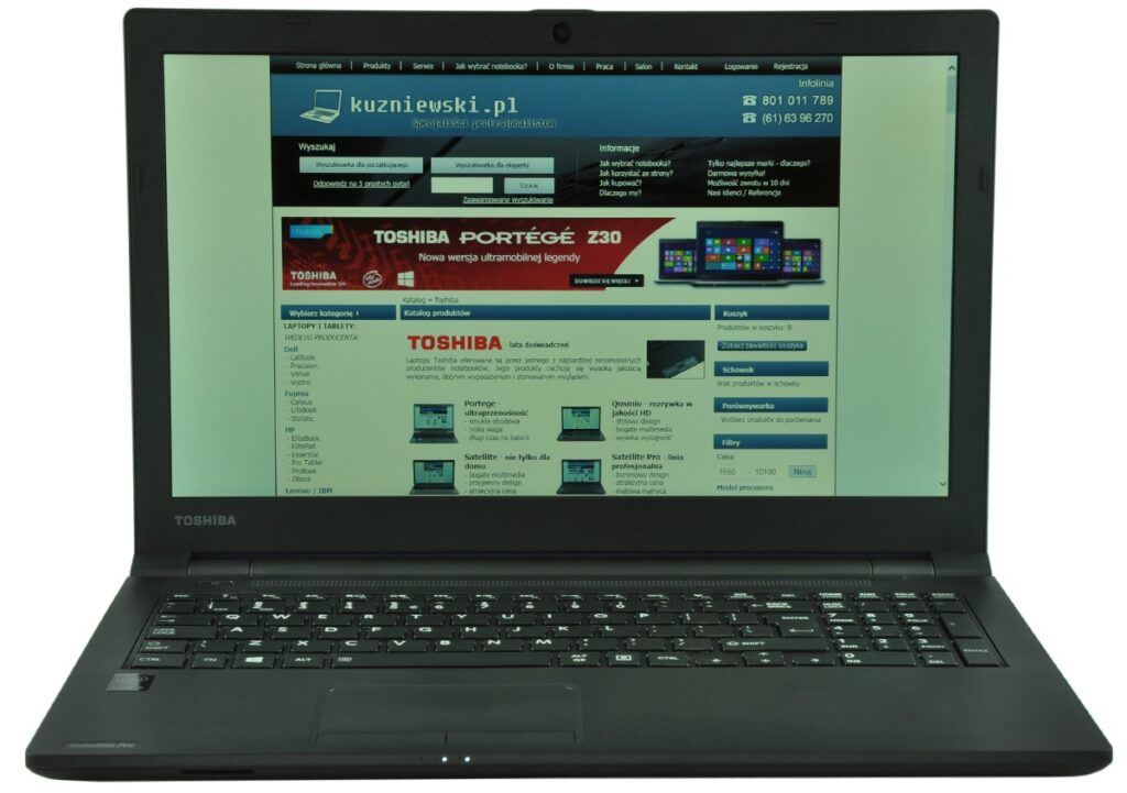 Black Toshiba laptop open, showing a Polish tech website on the screen with a blue header and navigation; Toshiba logo visible on the bottom bezel.