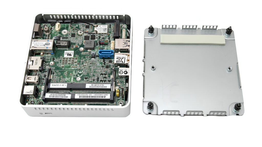 Open computer module showing a green motherboard with PCIe slots and connectors inside a small metal chassis, with the cover removed nearby.