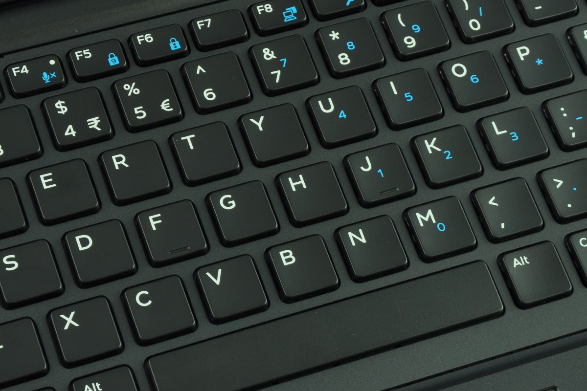 Close-up of a black laptop keyboard with white letters and blue secondary symbols on many keys, showing a standard QWERTY layout.
