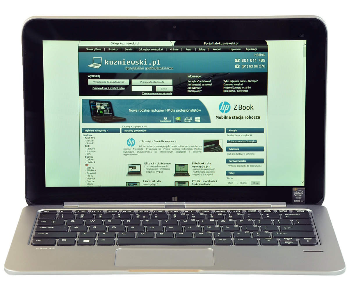 Silver laptop open, displaying a Polish tech website (kuzniewski.pl) on the screen with a blue header and navigation menu.
