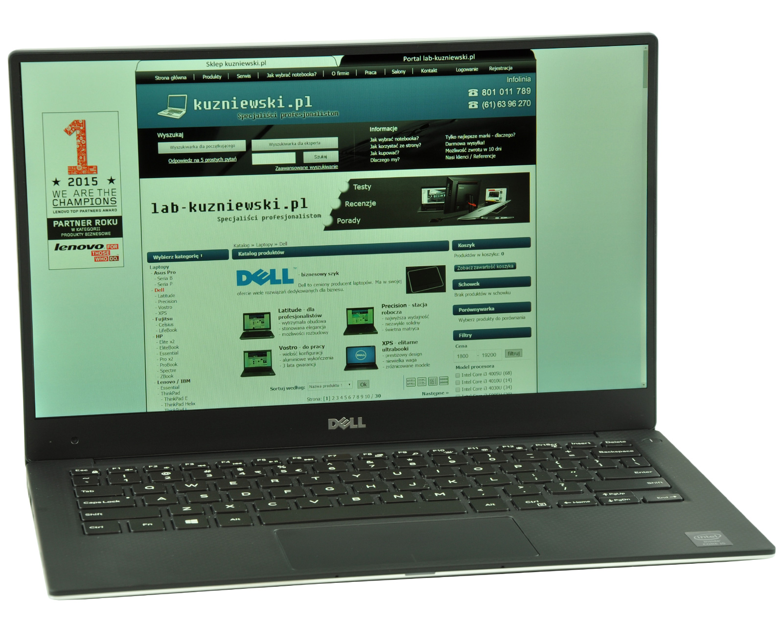 Dell laptop showing a Polish tech site (kuzniewski.pl) with teal header, left advertisement, and product grid on screen.