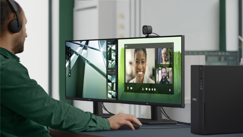 Dell_Pro_Slim_Essetnial_2026_1507_user02 - lab-kuzniewski.pl - Testy laptopów, recenzje i porównania Person with headset using a two-monitor desk setup, webcam mounted on the top monitor for a video call.
