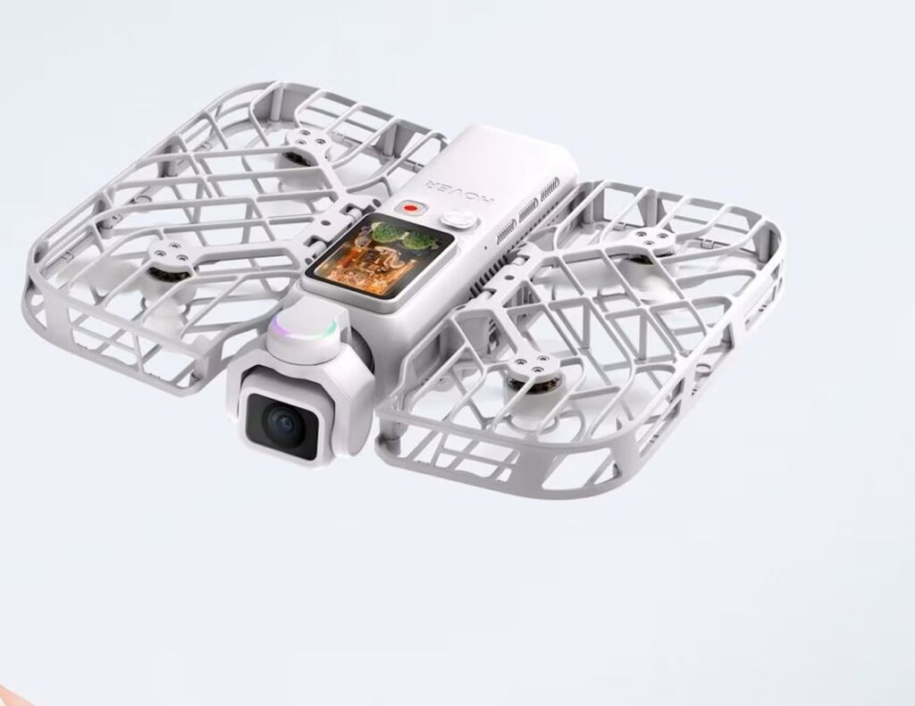 White quadcopter drone with protective lattice frame, front camera gimbal, and a small built-in screen on top of the body.