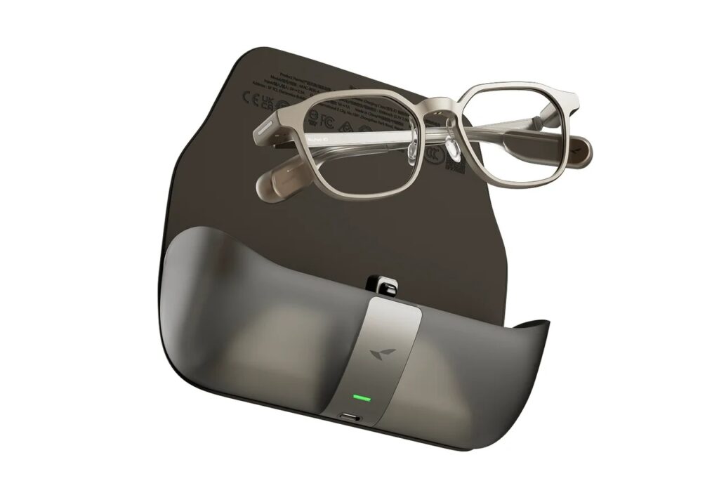 Pair of semi-transparent smart glasses resting on a curved dark charging case with a small green indicator light.