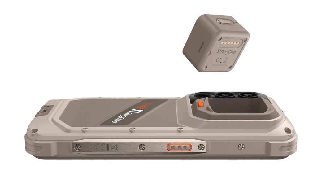 Rugged smartphone lying flat with a detachable cube battery module above, showing rugged ports and orange latch.