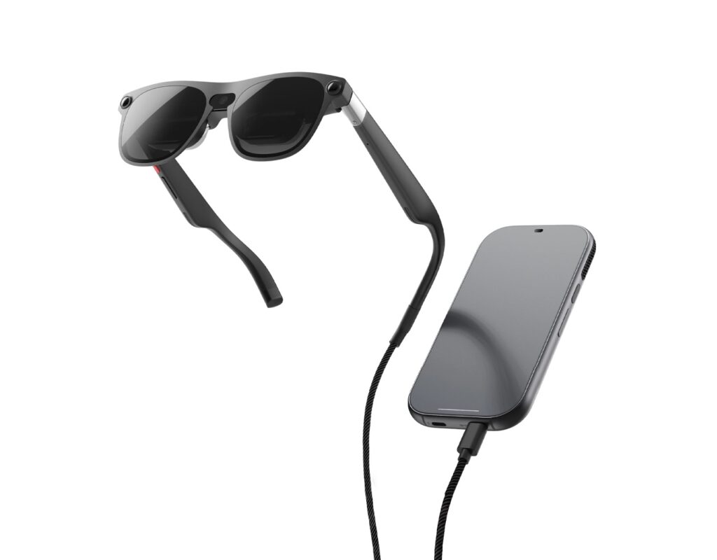 Black smart sunglasses suspended above a gray iPhone connected by a charging/data cable