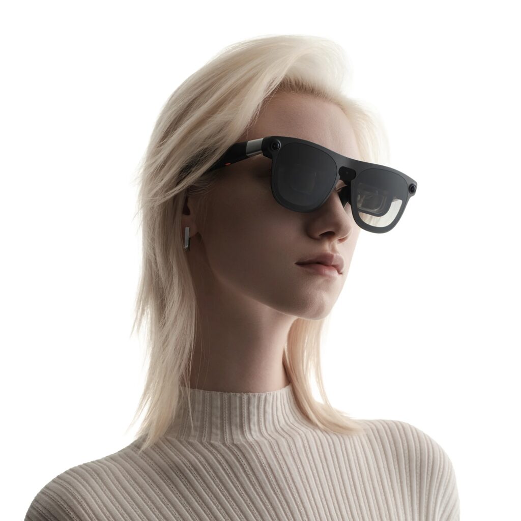 Portrait of a woman with platinum blonde hair wearing oversized black sunglasses against a white background, facing slightly right